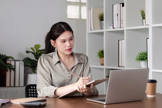 Young Asian business woman sitting in the office using a calculator to calculate business numbers..