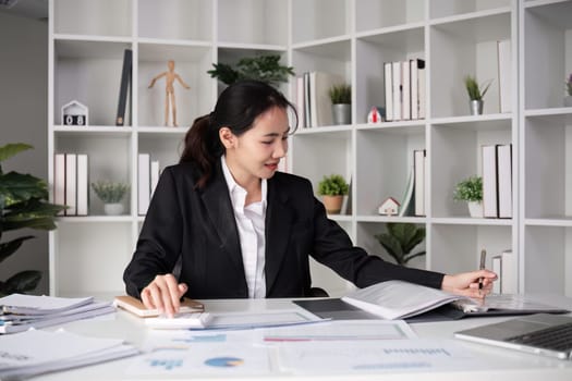 A young accountant calculates financial figures and company spending graphs using a calculator and laptop to take notes..