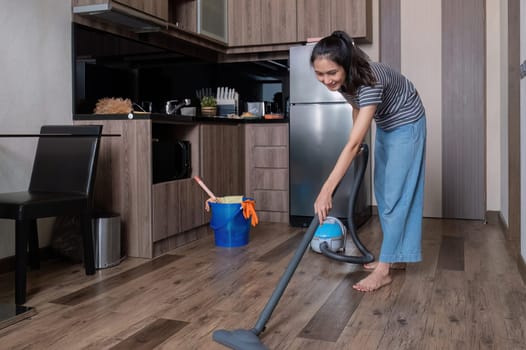 Young woman uses a vacuum cleaner to clean the kitchen floor. Cleaning the house during the holidays.