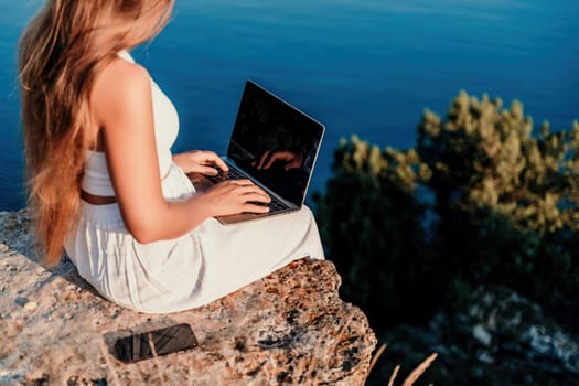 Freelance women sea working on the computer. Good looking middle aged woman typing on a laptop keyboard outdoors with a beautiful sea view. The concept of remote work