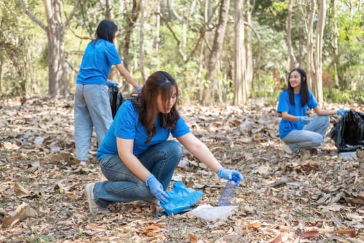 A group of Asian volunteers collects trash in plastic bags and cleaning areas in the forest to preserve the natural ecosystem..