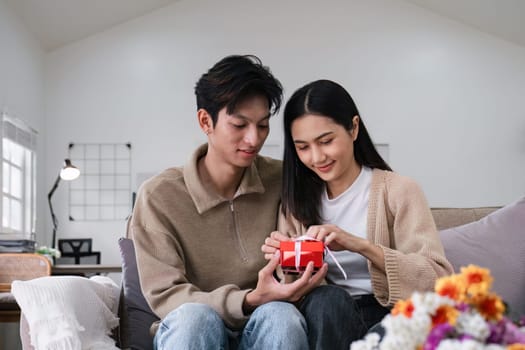 Young Asian couple giving each other giftbox on a special day. Sitting together happily in the living room.