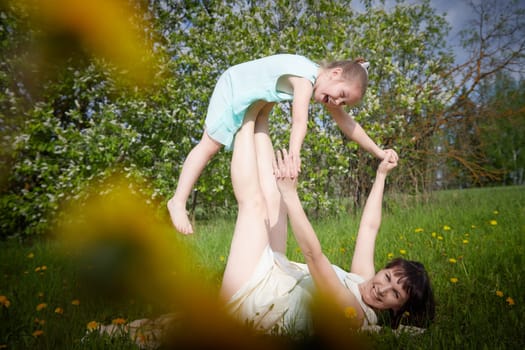 Happy mother and daughter enjoying rest, playing, fun and doing sports exercises on nature in a green field. Woman and girl resting outdoors in summer and spring day