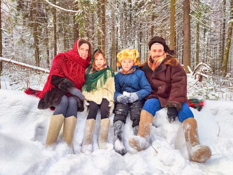 Joyful family ethnic dress with shawls and earflap hats in winter forest in carnival Maslenitsa in Russia. Tourists in Shrovetide in spring. Mother, father, son, daughter having fun in the snow