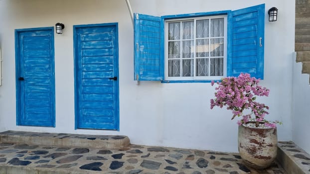 Bangsaray Pattaya Thailand 28 February 2024, A charming white house with vibrant blue shutters sits gracefully, accented by a flourishing potted plant.