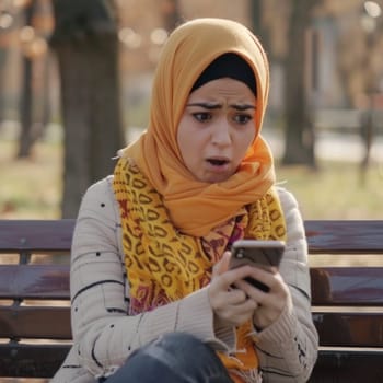 Arab girl is shocked and worried about negative news reading on the mobile phone while outdoors.
