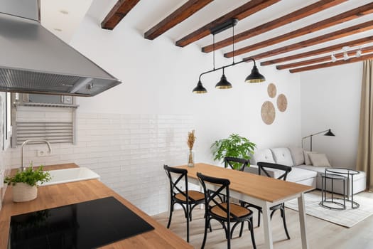 Horizontal shot of a loft-style kitchen-living room with a white wall of wooden beams with modern appliances, a dining table and a sofa corner in a relaxation area in a new apartment.