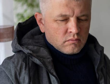 Portrait of the mid aged man with grey hair, wearing warm, dark blue sweater and grey coat.