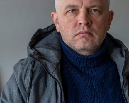 Portrait of the mid aged man with grey hair, wearing warm, dark blue sweater and grey coat.