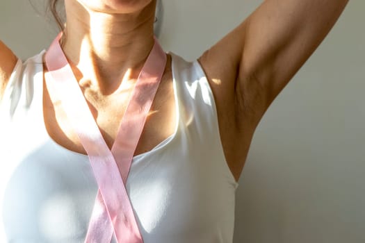 Shot of the woman in the white top against the white wall, with pink ribbon on her neck as a symbol of breast cancer awareness