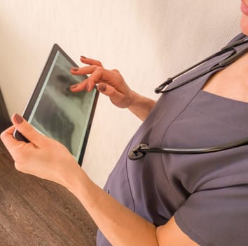 Shot of the female doctor in uniform against the white wall studying x-ray image of the lungs on the tablet