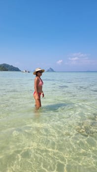 A graceful woman in a straw hat stands in the ocean, feeling the water embracing her feet as she connects with the sea in a serene moment. Koh Kradan Thailand