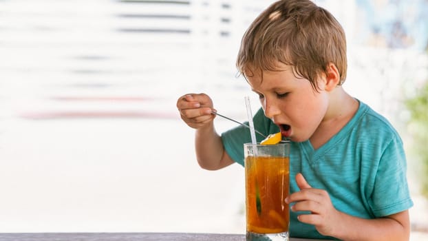 Happy childhood. Boy drinking fruit tea with ice in hot summer day time. Cute lover of sweets and tasty things.