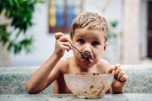 Happy childhood. Boy eating fruits with cacao spoon, summer day outside. Cute lover of sweets and tasty things .