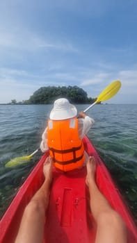 A person in a vibrant red kayak paddles gracefully towards a small, enchanting island in the distance, surrounded by calm waters. Koh Libong Thailand