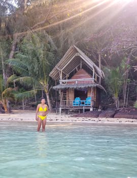 A woman in a yellow bikini stands gracefully in the water, the sunlight reflecting off the gentle waves around her. Koh Wai Thailand