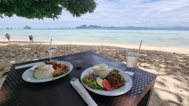 Two plates with delicious food beautifully arranged, sitting on top of a wooden table on the beach of Koh Kradan Thailand, Thai food