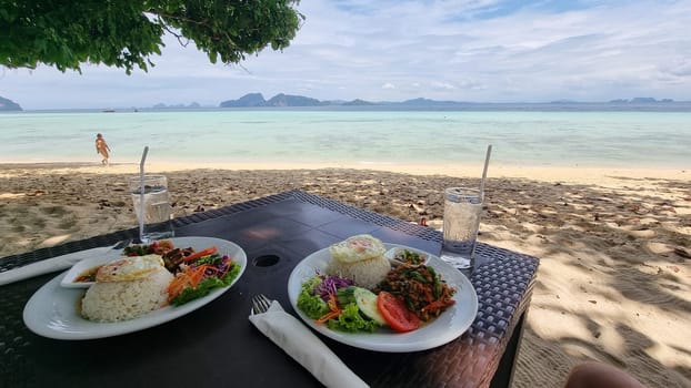 A tantalizing spread of freshly prepared dishes, served on elegant plates atop a rustic wooden table in a vibrant ocean beach setting, Thai food, Koh Kradan Thailand