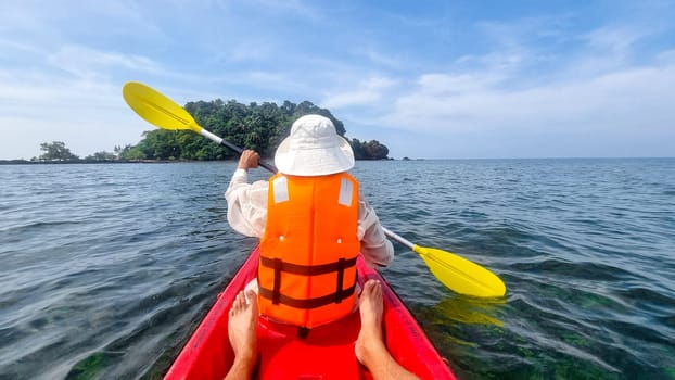 A person in a kayak paddles toward a small island, surrounded by calm waters and green foliage under a clear sky. Koh Libong Thailand women in kayak