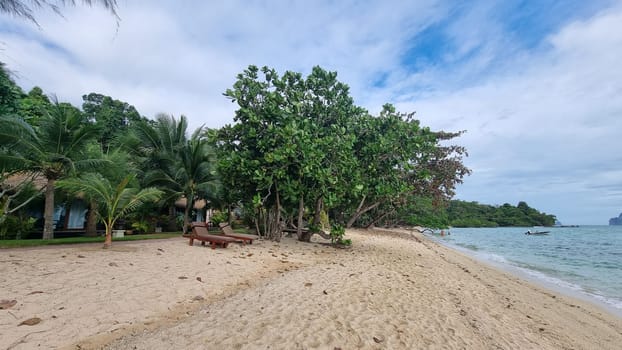 A tranquil sandy beach lined with lush trees and a charming house in the background under clear blue skies. Koh Kradan Thailand