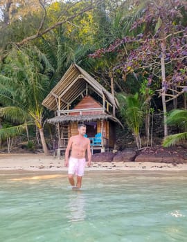 A man is peacefully standing in the water in front of a simple hut, surrounded by nature and tranquility. Koh Wai Thailand