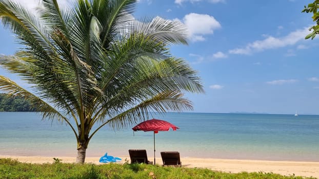 Two weathered chairs sit nestled under a vibrant red umbrella on a sandy beach, creating a cozy and inviting spot for relaxation and contemplation. Koh Libong Thailand