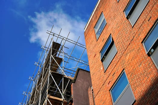 Looking up steel pipe scaffolding next to orange brick building against blue sky