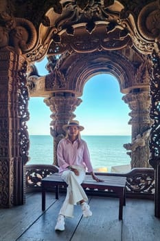 A women sits peacefully atop a weathered wooden bench, surrounded by the serenity of nature. Sanctuary of Truth Pattaya