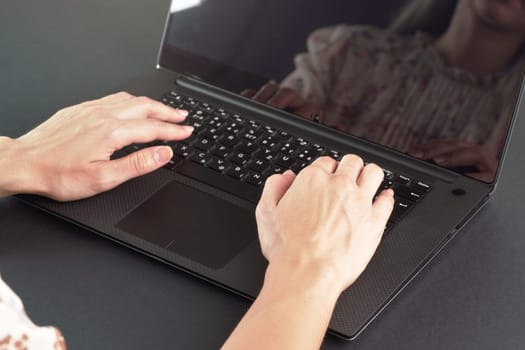 Young female working with laptop computer - detail on her hands over back keyboard