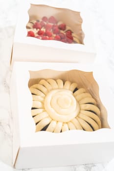 Two delightful homemade bundt cakes, each adorned with creamy cream cheese frosting, elegantly packaged in white paper boxes with a clear window to showcase their scrumptious appeal.