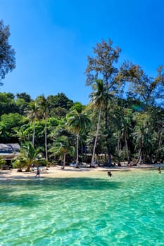 A picturesque beach dotted with lush trees and bustling with people enjoying the sun, sand, and surf. Koh Wai Thailand