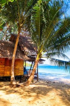 A traditional hut nestled on a sandy beach surrounded by tall swaying palm trees, radiating a feeling of peace and tranquility. Koh Wai Thailand