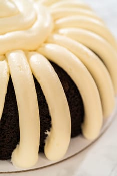 With precision, the Chocolate Bundt Cake is carefully removed from the pan - adorned with luscious cream cheese frosting, creating a delectable treat that is sure to delight.