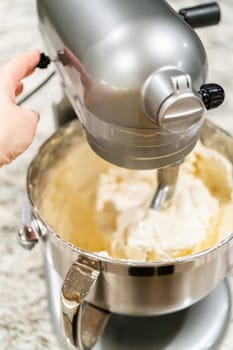 Stand mixer whips up creamy buttercream frosting to perfection, ready for dessert decorating.