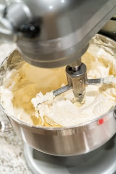 Stand mixer whips up creamy buttercream frosting to perfection, ready for dessert decorating.