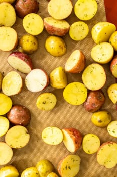 In a modern kitchen, an array of halved, multicolored marble potatoes are arranged on a baking pan lined with a silicone liner. The roasting process infuses the kitchen with a mouthwatering aroma, indicating a delicious side dish in the making.