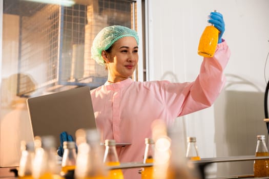 Quality inspector a woman carefully examines beverage bottles on a conveyor belt in the factory. Using a laptop she ensures stringent liquid quality standards.