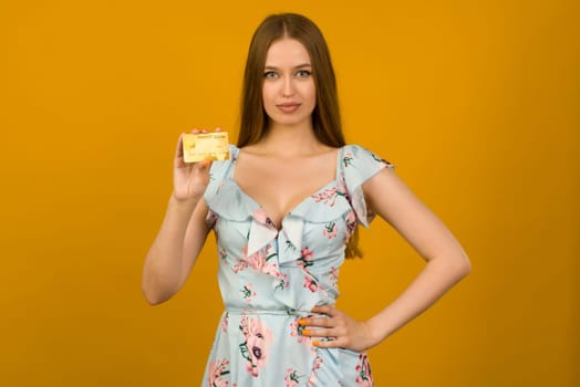 Photo of pleased young woman posing isolated over yellow wall background holding debit or credit card.