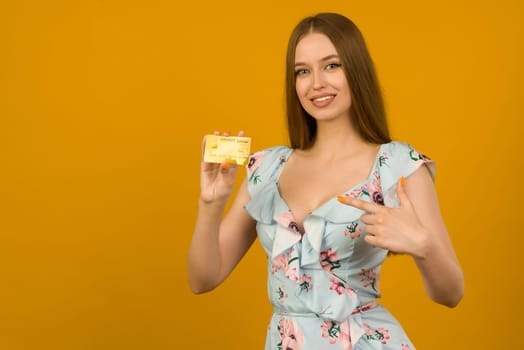 Photo of pleased young woman posing isolated over yellow wall background holding debit or credit card.