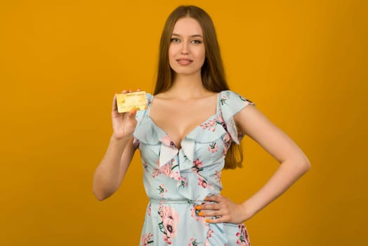 Photo of pleased young woman posing isolated over yellow wall background holding debit or credit card.