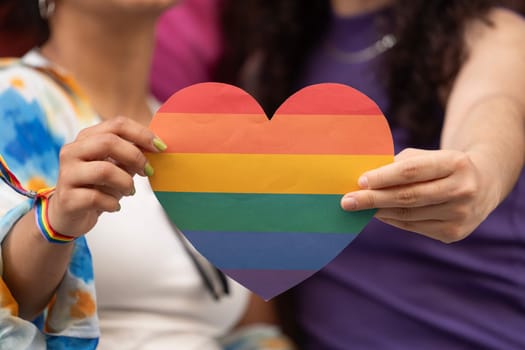 Lesbian women couple holding a heart with rainbow colors as heterosexual love sign.