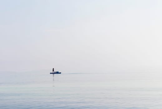 Shot of a man on a small catamaran boat by the horizon, which is hard to detect because of the fog and humidity