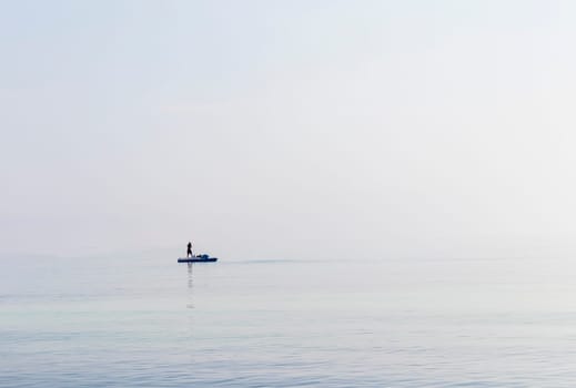 Shot of a man on a small catamaran boat by the horizon, which is hard to detect because of the fog and humidity