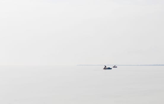 Shot of a man on a small catamaran boat by the horizon, which is hard to detect because of the fog and humidity