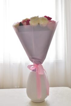 A bouquet of flowers in a ceramic vase stands on a table in the room