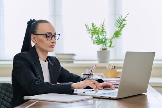 Business woman working in home office at desk with laptop computer. Serious 30s female typing looking at monitor. Remote business, technologies, internet, teaching, blogging, work, freelance concept