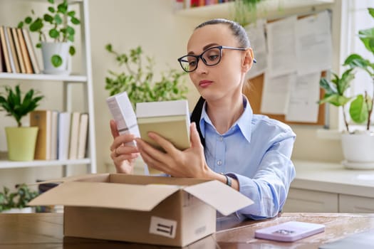 Satisfied female consumer buyer sitting at home unpacking cardboard box with online purchases. Woman unpacking boxes with cosmetics care products perfumes. Delivery by mail, internet online store