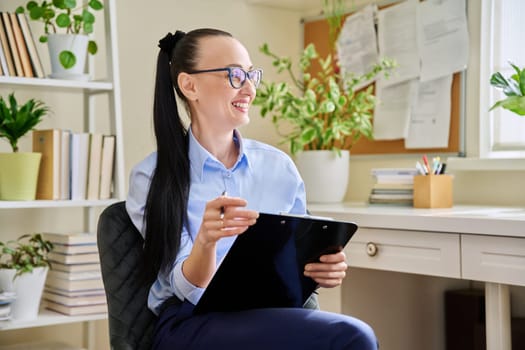 Portrait of happy smiling female psychotherapist with clipboard at workplace in office. Professional mental therapist, counselor, psychologist, social worker. Health care service psychology treatment