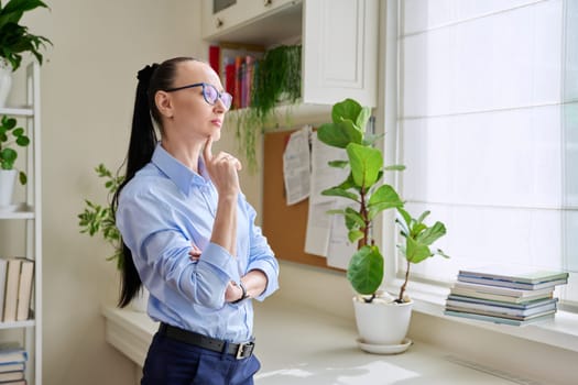 Serious thoughtful woman in her 30s looking out the window. Emotions, lifestyle, health, people concept