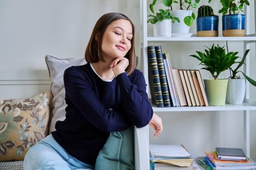 Portrait of young attractive smiling woman in home interior. Happy cheerful relaxed 20s female looking away, sitting on couch. Beauty, youth, happiness, health, lifestyle concept